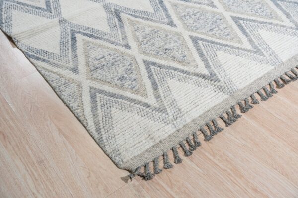Thick pile rug with gray geometric diamonds on a cream background and gray tassels, resting on light wood flooring.
