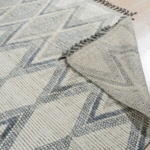 High-texture, cream and gray geometric rug with a folded corner on light wood flooring.