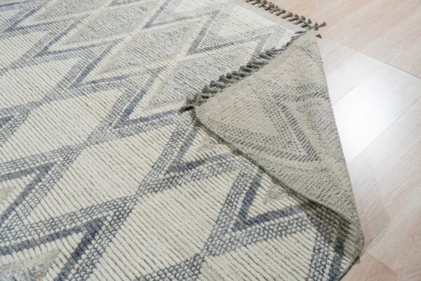 High-texture, cream and gray geometric rug with a folded corner on light wood flooring.