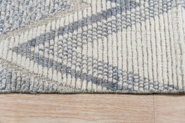 High-pile rug detail showing ribbed texture and a diagonal pattern in white, blue, and gray on a wood floor.