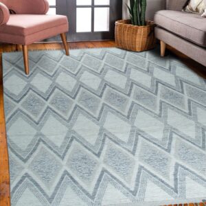 Pale blue geometric rug with tassels on wood floor next to a pink chair and gray couch.