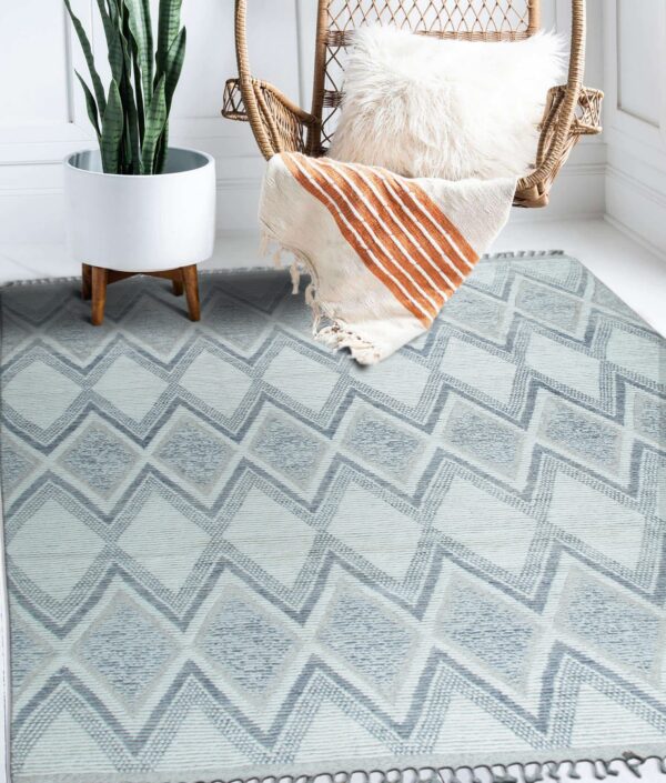Blue and white geometric diamond rug on a white floor next to a wicker chair and large potted plant.