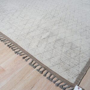 A cream high-pile rug with subtle geometric patterns and gray tassels rests on light wood flooring.