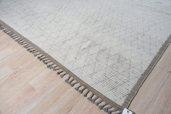 A cream high-pile rug with subtle geometric patterns and gray tassels rests on light wood flooring.