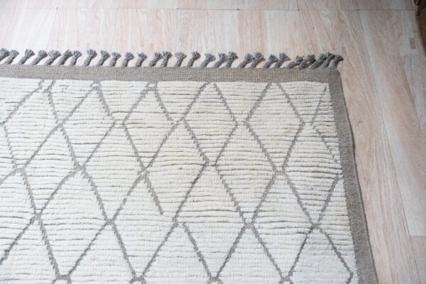 High-pile cream rug with gray diamond pattern and tassels rests on light wood-look flooring.