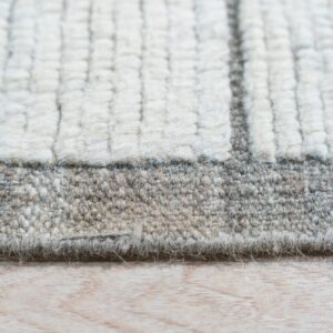Highly textured cream and gray striped rug edge transitioning to a dense low pile border on light wood floor.