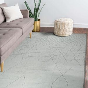 Pale low-pile rug with abstract geometric line patterns displayed in a room with a gray sofa and woven pouf.