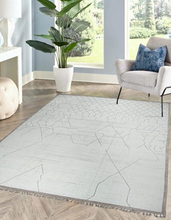 Flatwoven light gray rug featuring a dark geometric pattern in a bright room with an armchair and plant.
