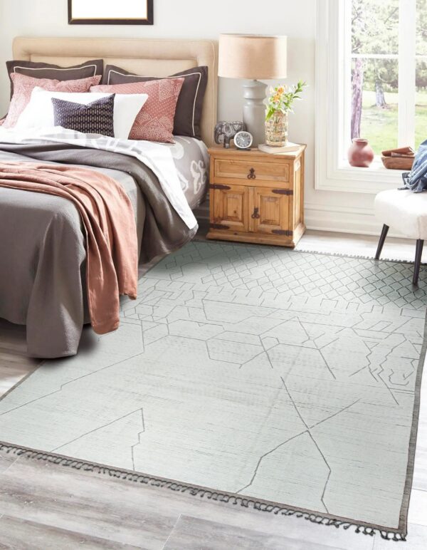 Light gray flatweave rug with abstract pattern defines a cozy bedroom beside a window.