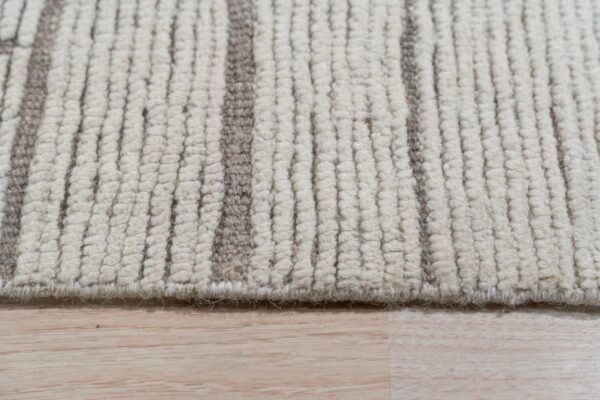 Closeup of a chunky ivory looped pile rug with vertical taupe stripes, resting on light plank wood flooring.