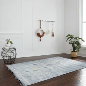 A flatwoven blue and white abstract rug with fringe lies on dark hardwood flooring.