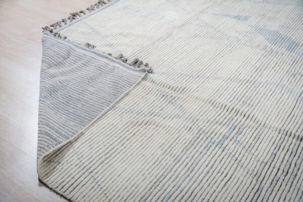 High-pile cream ribbed rug with subtle blue pattern, folded to show the striped flat-woven backing.