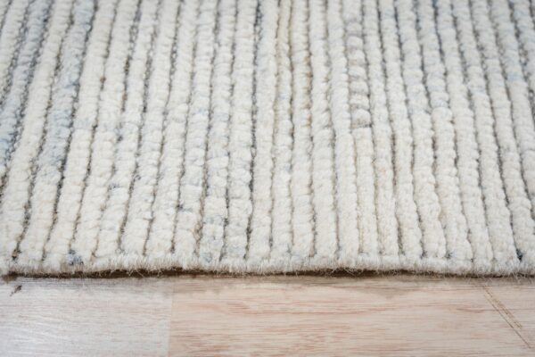 High-pile cream rug with raised vertical ribs and gray flecks sits on light wood planks.