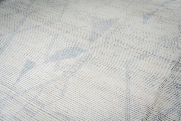 White textured rug features strong horizontal ribbing and subtle blue abstract geometric shapes.