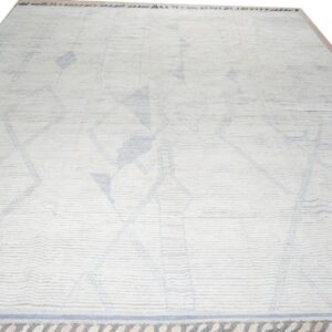 A ribbed cream rug features light blue abstract diamond patterns and a darker blue tasseled border.