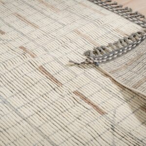 Ribbed cream rug with thick pile, grey and brown accents, and a folded corner showing grey tassels on wood floor.