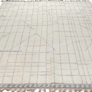 Off-white high-pile rug with blue-gray geometric grid pattern and gray tasseled fringe.