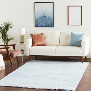 Low-pile light blue rug with a diamond pattern and pom-pom trim beneath a white couch.