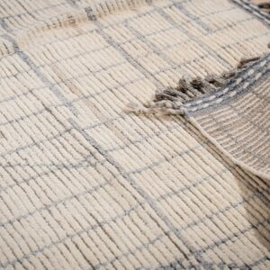 Close-up of a shaggy cream rug with a blue grid, showing the fringed edge and woven backing on wood flooring.
