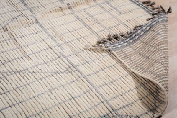 Close-up of a shaggy cream rug with a blue grid, showing the fringed edge and woven backing on wood flooring.