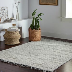 Woven light grey rug featuring a checkered design and dark tassels rests on dark hardwood flooring.