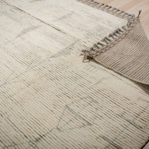 Textured cream rug with gray accents, curled to show the striped woven backing on light wood floor.