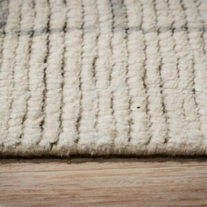 Detailed view of a cream, high-pile textured rug showing ribbed texture and faint dark accents over wood flooring.