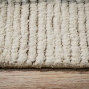 Close-up of textured cream rug rows with dark vertical stripes on light wood grain.