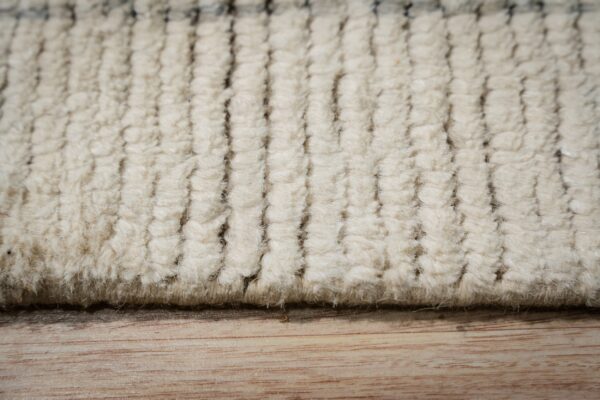 Close-up of textured cream rug rows with dark vertical stripes on light wood grain.
