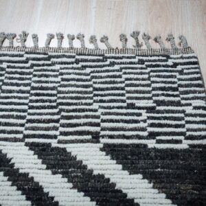 Chunky black and white geometric rug with short braided tassels visible on light wood planks.