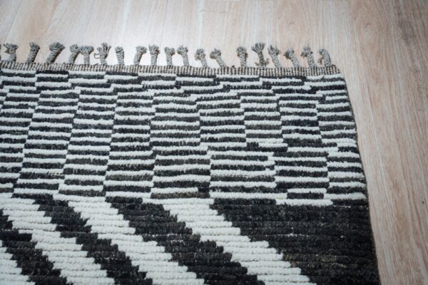 Chunky black and white geometric rug with short braided tassels visible on light wood planks.