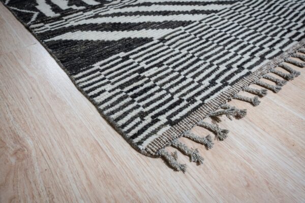 High-pile black and off-white rug with bold geometric patterning and knotted fringe on light wood.