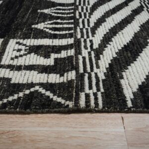 Close-up of a high pile dark gray and cream geometric rug resting on light wood flooring.
