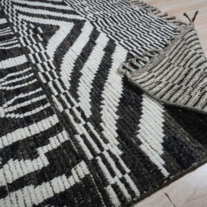 Close-up of a high-pile rug with dark geometric patterns on cream, folded over light wood flooring.