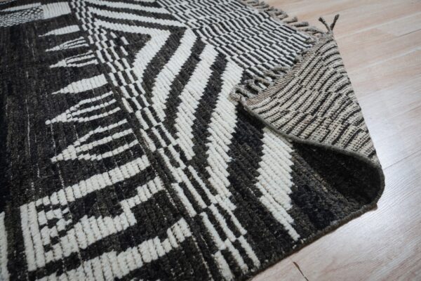 Close-up of a high-pile rug with dark geometric patterns on cream, folded over light wood flooring.