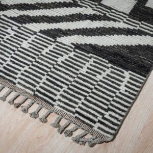 High-pile rug with dark geometric stripes and gray tassels on a cream field, placed on light wood flooring.