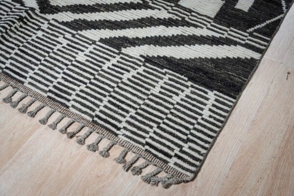 High-pile rug with dark geometric stripes and gray tassels on a cream field, placed on light wood flooring.