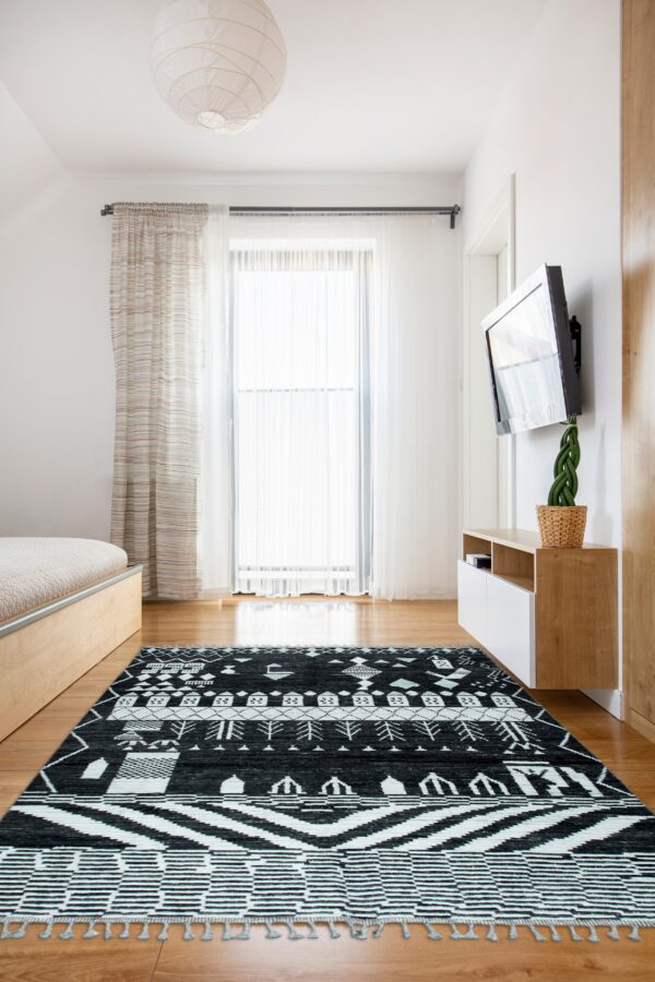 Black and white low-pile rug with tribal geometric patterns rests on wood floors in a bright bedroom.