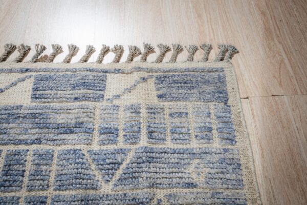 Textured beige rug with high-pile blue geometric patterns and fringe on light wood flooring.