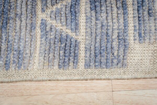 Blue high-low pile rug detail against a cream flat weave, resting on light wood flooring.