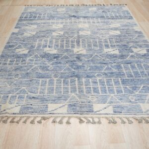 Textured blue and cream rug with geometric striped patterns and tassels lying on light wood flooring.