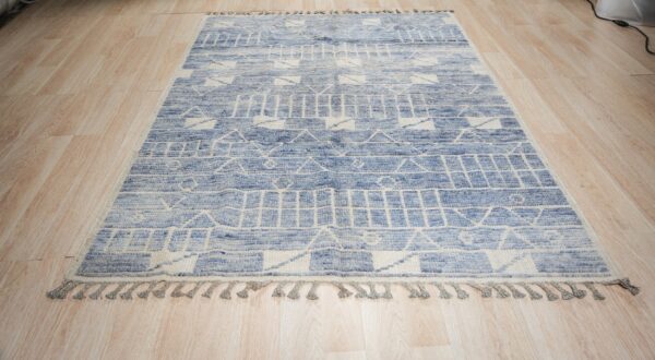 Textured blue and cream rug with geometric striped patterns and tassels lying on light wood flooring.