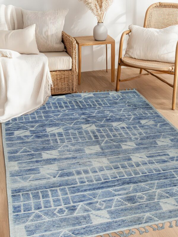 A faded blue geometric rug with tassels anchors a bright sitting area with wicker furniture.