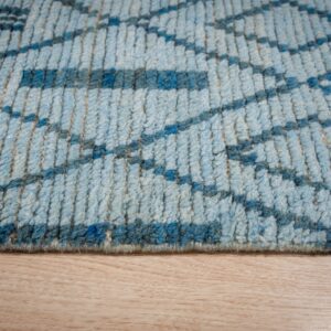High-pile blue rug with a geometric pattern rests against light blonde wood flooring.