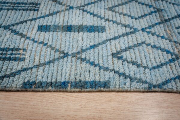 High-pile blue rug with a geometric pattern rests against light blonde wood flooring.