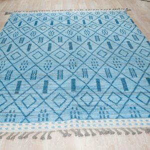 Blue high-pile rug with geometric diamond and stripe motifs, fringed ends, displayed on wood planks.