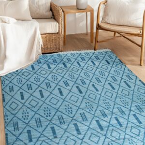 Flat-woven light blue rug with dark blue geometric patterns and tassels sits between rattan seating.