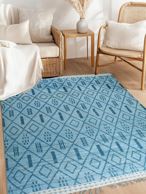 Flat-woven light blue rug with dark blue geometric patterns and tassels sits between rattan seating.