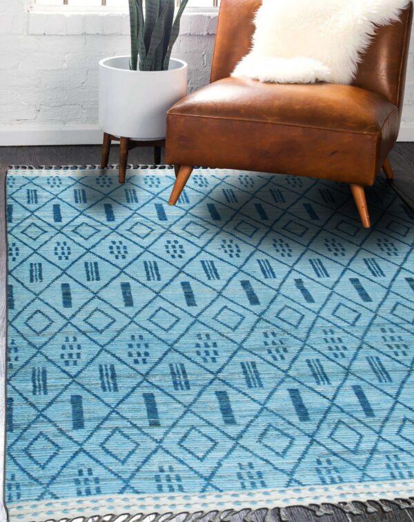 Blue geometric patterned rug on dark flooring beneath a caramel leather chair and potted plant.