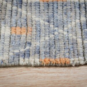 Close-up of a high-pile, textured rug featuring abstract blocks of blue, cream, and orange on light wood flooring.